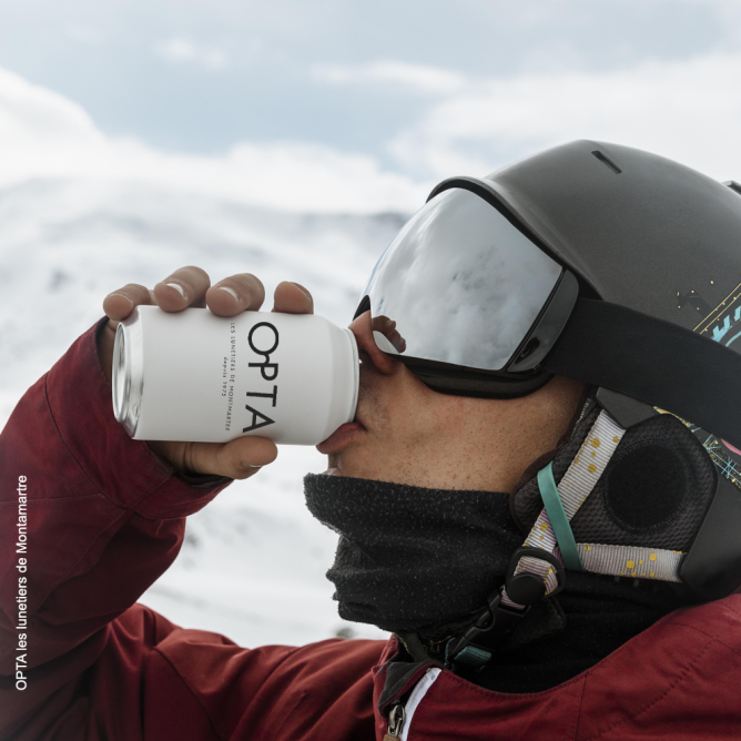 Skieur avec un masque de ski buvant une cannette de soda avec le logo de OPTA